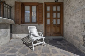 A stone-paved courtyard with a white chair, wooden shutters, and a double door. - AffittiPontediLegno - Casa Ruby (Ponte di legno)