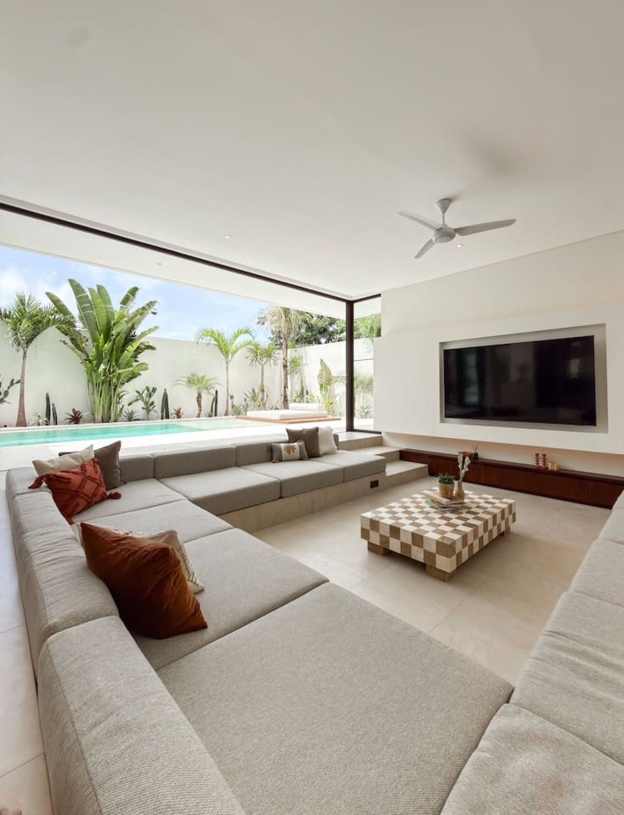 Ein modernes Wohnzimmer mit großem Fernseher, bequemen Sitzmöglichkeiten und Blick auf einen Pool.