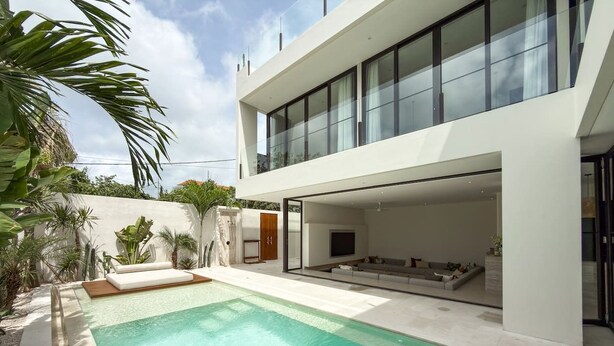Una casa moderna con piscina, un área de estar cubierta al aire libre y un amplio salón con ventanales.