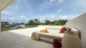 A rooftop terrace with a sofa, a large vase, and a bowl of fruit.