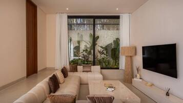 A modern living room with a sectional sofa, a flat-screen TV, and a large window with a view of greenery.