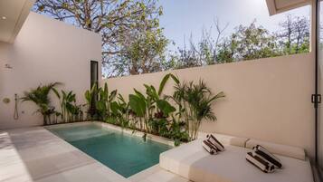 A modern outdoor pool area with a white tiled floor, a beige wall, and a variety of tropical plants.
