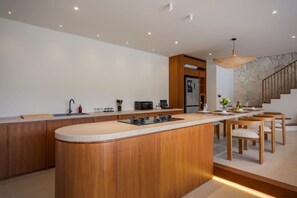 A modern kitchen with a central island, wooden cabinets, and a stone accent wall. - NEW 4BR Luxury Villa in the Heart of Bingin (South Kuta)
