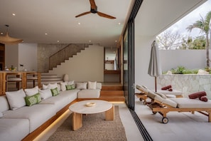 A modern living room with a sectional sofa, a coffee table, and a sun lounger by a glass wall. - NEW 4BR Luxury Villa in the Heart of Bingin (South Kuta)