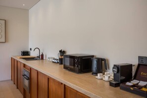 A modern kitchen with a built-in oven, a microwave, a coffee maker, and a coffee station with cups and a box of coffee beans. - NEW 4BR Luxury Villa in the Heart of Bingin (South Kuta)