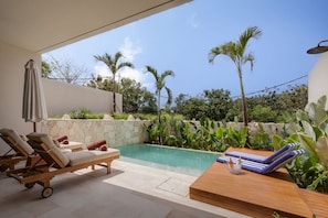 A poolside area with lounge chairs, a wooden table, and a stone wall. - NEW 4BR Luxury Villa in the Heart of Bingin (South Kuta)