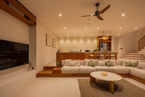 A modern living room with a sectional sofa, a coffee table, a TV, and a dining area with a kitchen in the background. - NEW 4BR Luxury Villa in the Heart of Bingin (South Kuta)