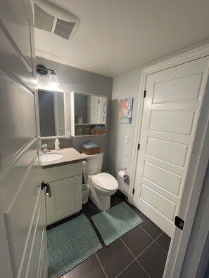 Un baño con inodoro, lavamanos, espejo y armario de almacenamiento.