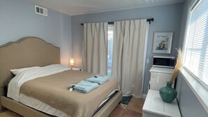 Een hotelkamer met een bed, bureau, stoel, raam met gordijnen, een foto aan de muur en een plafondlamp.