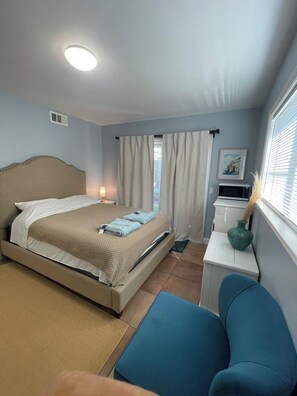 Habitación de hotel con cama, escritorio, silla, ventana con cortinas, un cuadro en la pared y una lámpara en el techo.