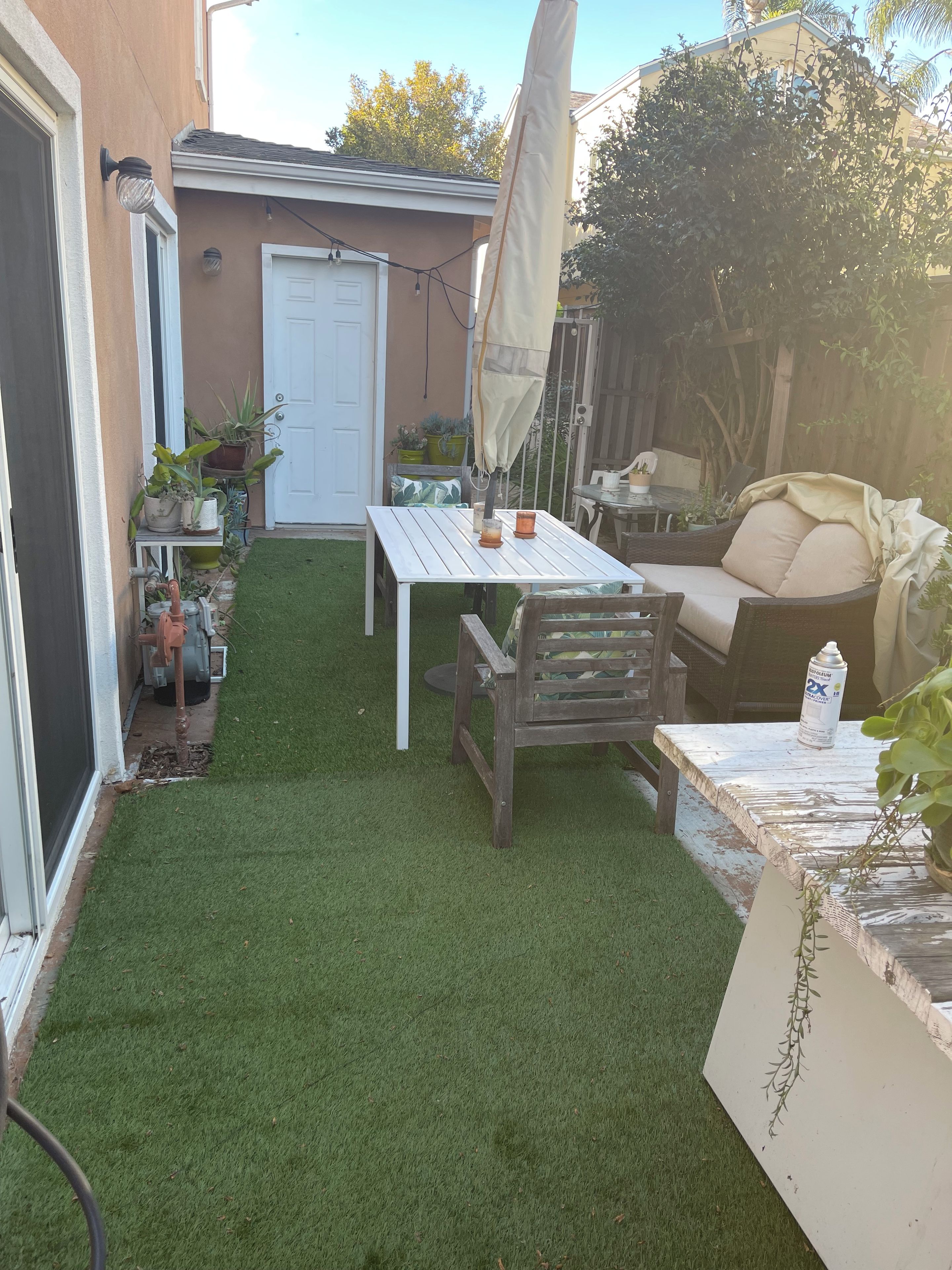 A backyard with a white table, a wooden chair, and a covered umbrella.