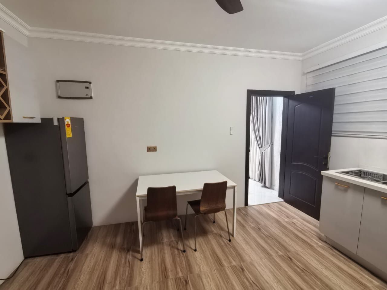 A compact kitchen with a dining area, a black refrigerator, and a door leading to a balcony.