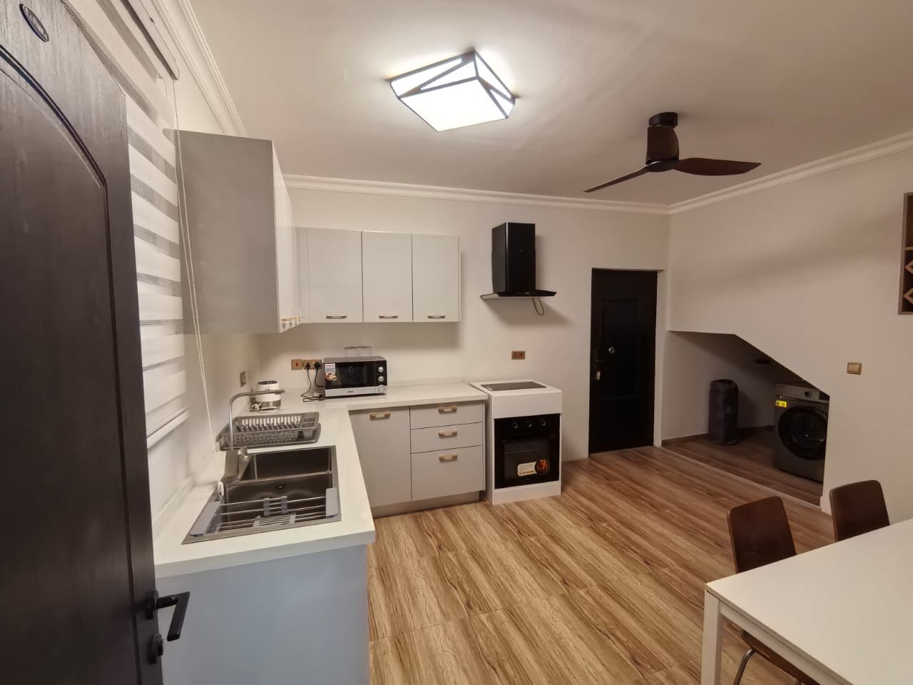 A compact kitchen with a microwave, toaster, and oven, a dining area with a table and chairs, and a ceiling fan.