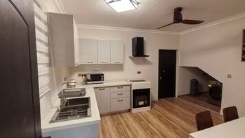 A compact kitchen with a microwave, toaster, and oven, a dining area with a table and chairs, and a ceiling fan.