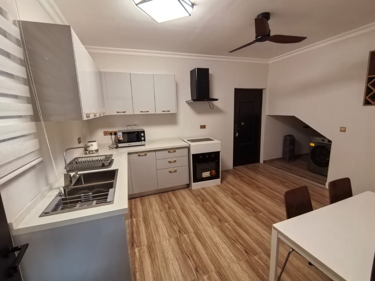 A compact kitchen with a microwave, stove, and sink, a dining area with a table and chairs, and a ceiling fan.