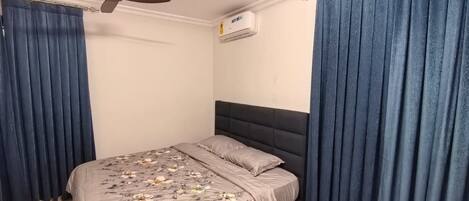 A bedroom with a bed, curtains, a ceiling fan, and an air conditioning unit.