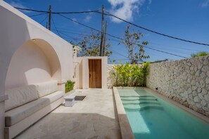 Ein privater Poolbereich mit einer Steinmauer, einer Holztür und einem weißen Outdoor-Sofa.