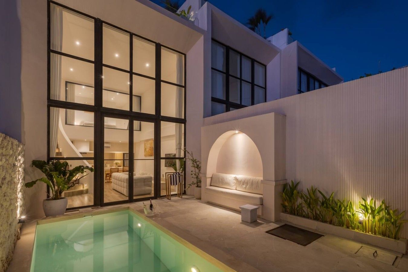Ein modernes Haus mit Swimmingpool, großen Fenstern und einem gut beleuchteten Sitzbereich im Freien.