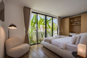 Ein modernes Schlafzimmer mit einem großen Bett, einer Couch, einer Stehlampe und Blick auf Grün durch eine Glasschiebetür.