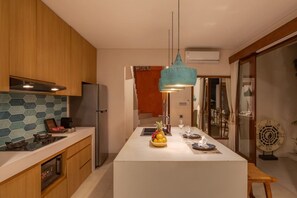 A modern kitchen with a central island, wooden cabinets, a stainless steel refrigerator, and a teal pendant light. - 1BR Ocean View Villa w/ Pool – Bingin (South Kuta)