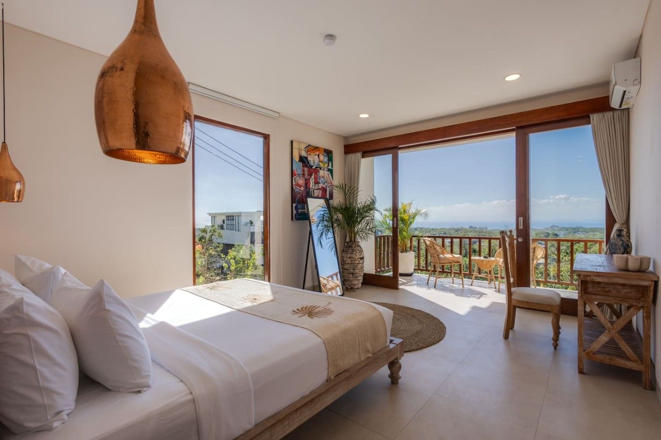 Une chambre d’hôtel avec un lit, un balcon doté d’une table et de chaises, et un tableau accroché au mur.