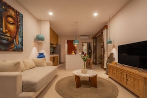 A modern living room with a sofa, a coffee table, a TV, and a painting on the wall. - 1BR Ocean View Villa w/ Pool – Bingin (South Kuta)