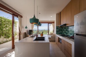 A modern kitchen with a central island, pendant lighting, and a view of greenery outside. - 1BR Ocean View Villa w/ Pool – Bingin (South Kuta)