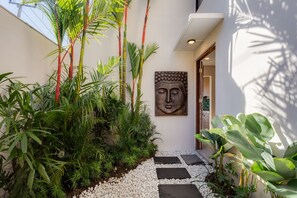A modern interior with a stone pathway leading to a door, surrounded by lush greenery and a Buddha statue. - 1BR Ocean View Villa w/ Pool – Bingin (South Kuta)