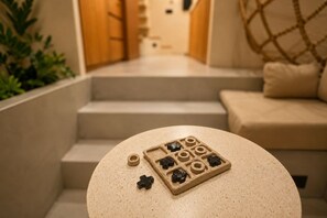 Ein runder Tisch mit einem Spielbrett und Spielfiguren, eine Treppe zu einer Sitzgruppe und eine Pflanze im Vordergrund.