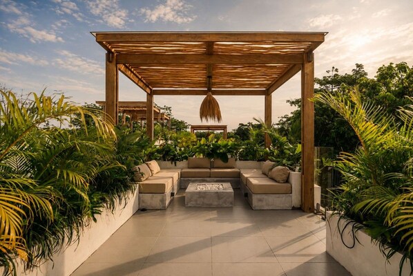 Ein überdachter Außenbereich mit Holz-Pergola, gepolsterten Sitzgelegenheiten und Pflanzen in Töpfen.