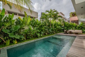 A swimming pool with a wooden deck, surrounded by lush tropical plants and modern buildings. - Kulu Villa 4BR Luxury Villa with Rooftop - Uluwatu (South Kuta)