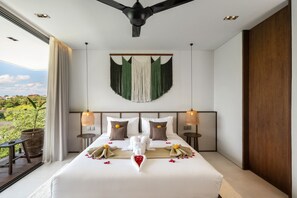 Une chambre d’hôtel avec un grand lit, deux tables de chevet, un ventilateur de plafond et une vue sur la verdure.