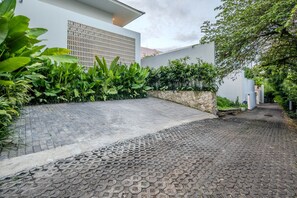 Une allée pavée mène à un bâtiment moderne doté d’un mur en pierre et d’une végétation luxuriante.