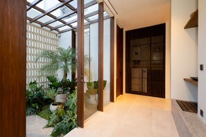 Un intérieur moderne avec une porte en verre donnant sur une véranda luxuriante, remplie de plantes.