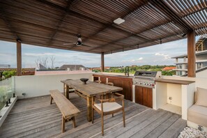 An outdoor patio with a wooden table and benches, a grill, and a view of the surrounding neighborhood. - Kulu Villa 4BR Luxury Villa with Rooftop - Uluwatu (South Kuta)