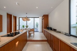 A modern kitchen with a central island, wooden cabinetry, and a stone backsplash. - Chianti 2BR Luxury Villa in the Heart of Bingin (South Kuta)
