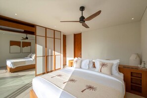 Een hotelkamer met een groot bed, een plafondventilator, een houten garderobe en een klein tafeltje met een vaas.