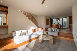 A modern living room with a sectional sofa, a wooden staircase, and a view to the outdoors. - Chianti 2BR Luxury Villa in the Heart of Bingin (South Kuta)