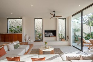 A spacious living room with a large sofa set, a coffee table, and a flat-screen TV mounted on a stone wall. - Chianti 2BR Luxury Villa in the Heart of Bingin (South Kuta)