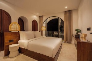 A modern bedroom with a large bed, two bedside lamps, a wooden headboard, a round bedside table, and a view through a glass door. - Kaia 1BR Villa in the Heart of Bingin, Uluwatu (South Kuta)