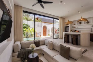 A modern living room with a sofa, TV, and a view of a pool and outdoor area. - Kaia 1BR Villa in the Heart of Bingin, Uluwatu (South Kuta)