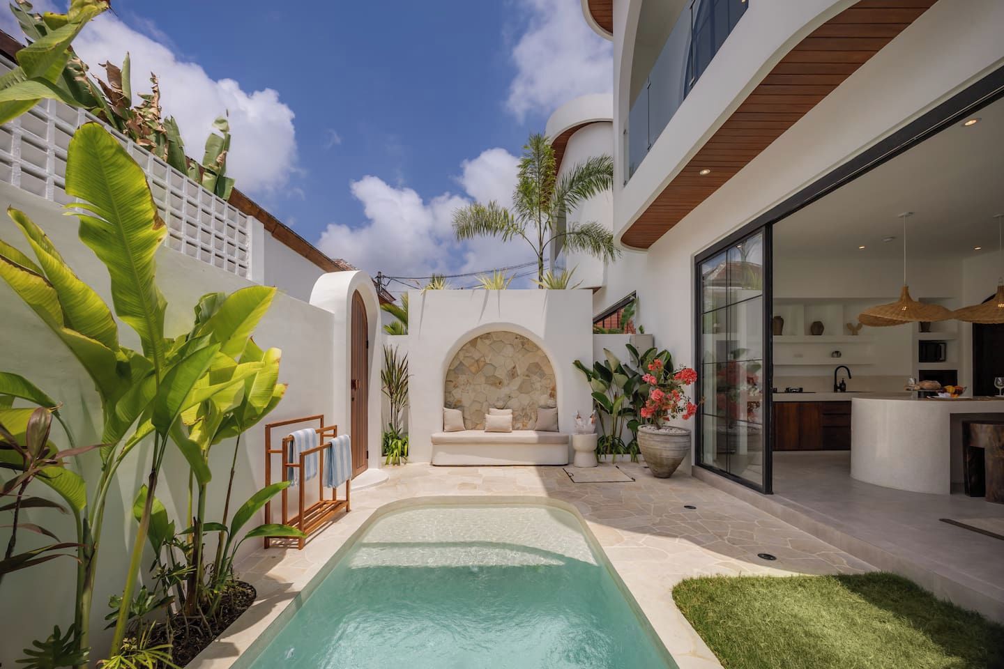 A modern house with a pool, a stone archway, and a kitchen visible through glass doors.