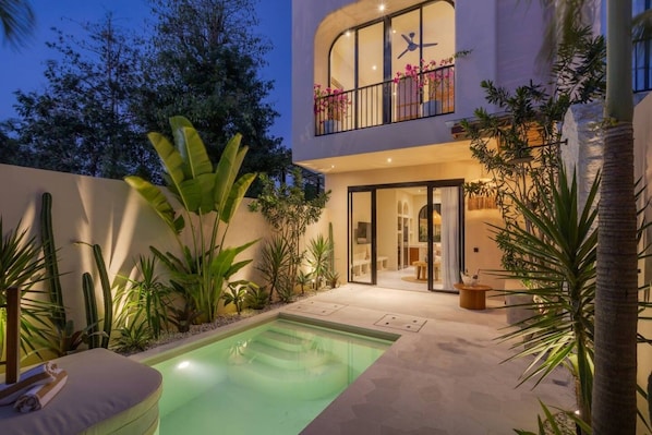Una casa moderna con piscina, mobiliario exterior y abundante vegetación.