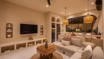 A modern living room with a flat-screen TV, a sofa, a coffee table, and a dining area with a kitchen counter.