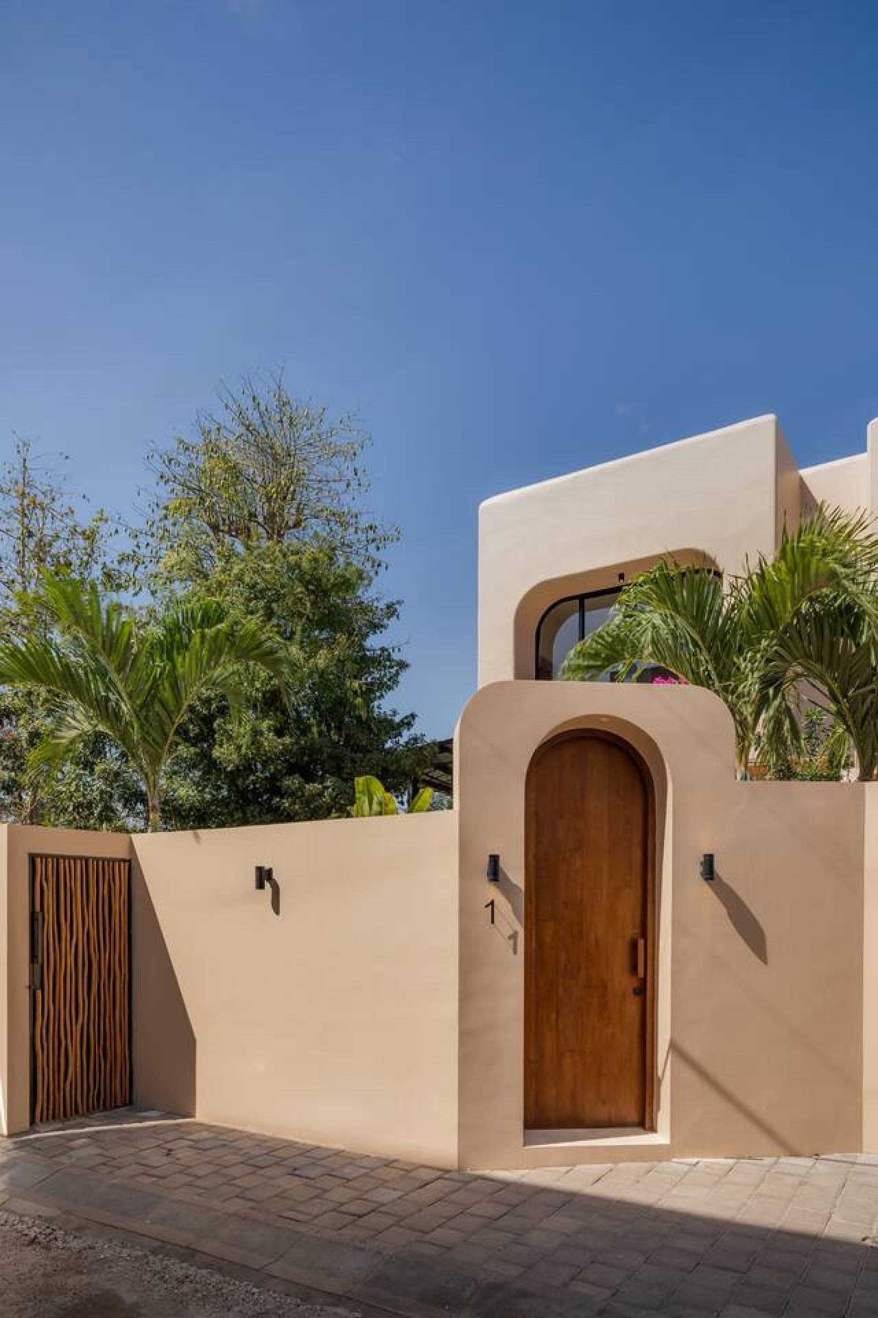 Un bâtiment moderne avec une porte en bois, une plaque portant le chiffre « 1 » et un luminaire fixé au mur.