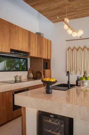 A modern kitchen with wooden cabinets, a built-in dishwasher, a marble countertop, and a hanging light fixture. - Roya 2BR Private Pool Villa w/ Jacuzzi in Bingin (Uluwatu)