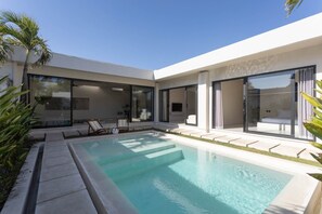 A modern poolside area with a clear pool, lounge chairs, and a glass-enclosed patio. - Vega 2BR Luxury Private Pool Villa - Ungasan (South Kuta)