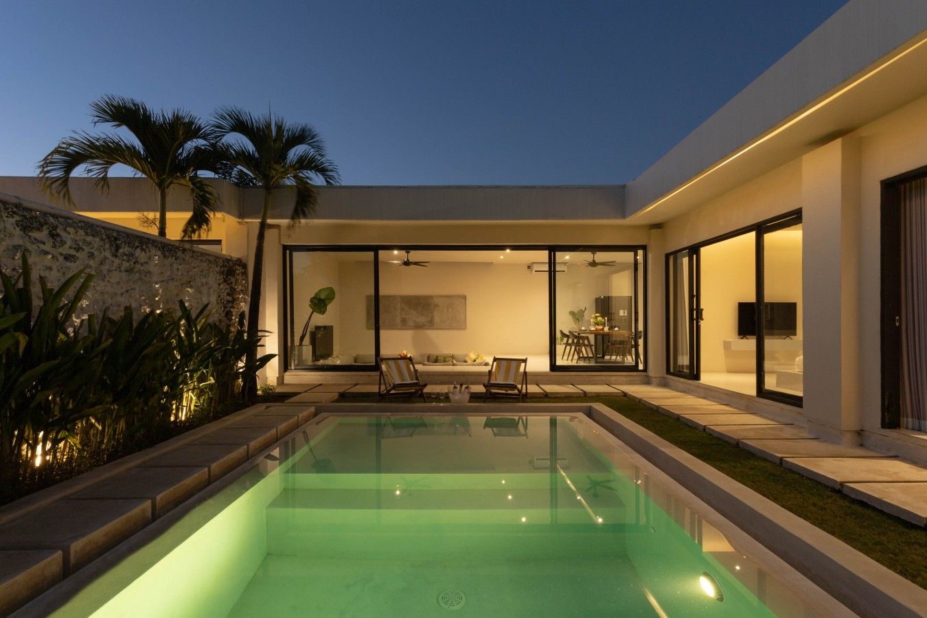 A modern house with a swimming pool, glass doors leading to a dining area, and a well-maintained lawn.