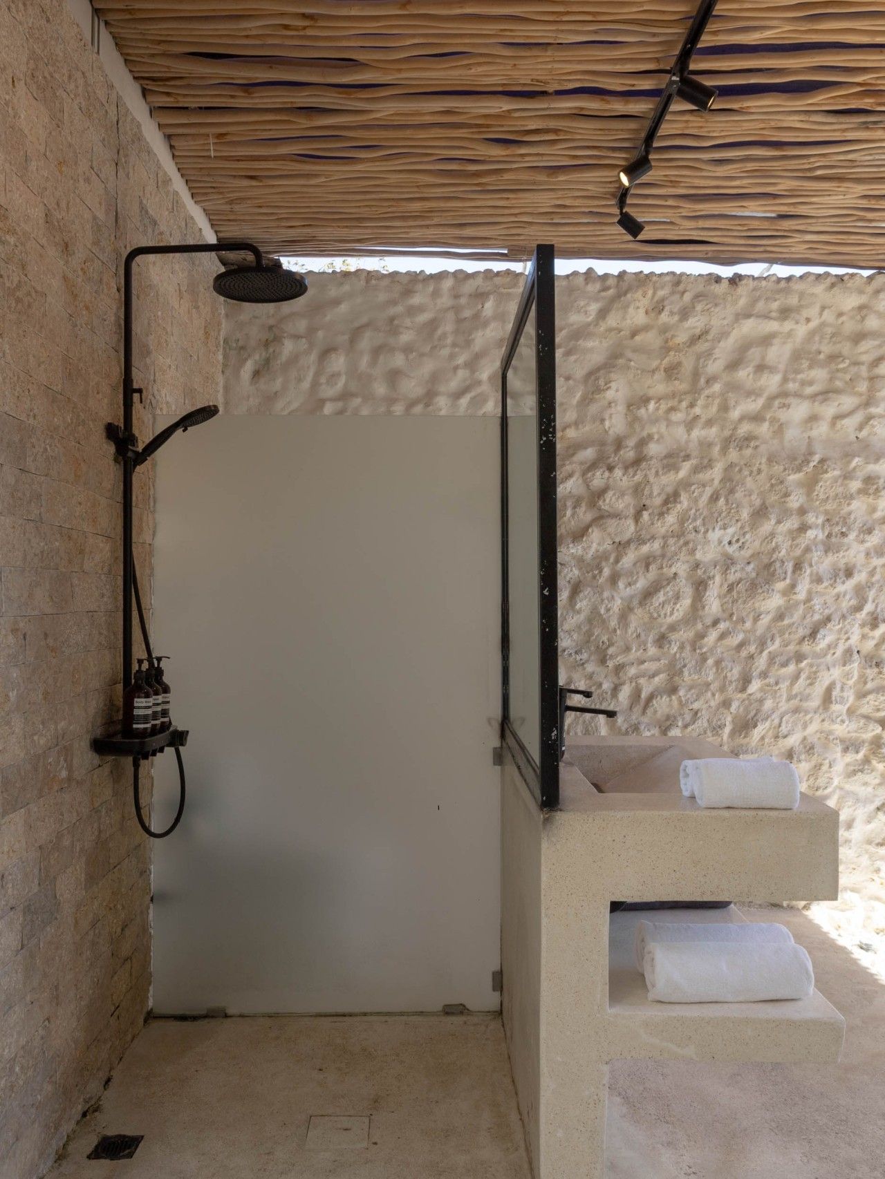 A small, enclosed shower area with a wooden ceiling, a white door, and a concrete sink with two towels.