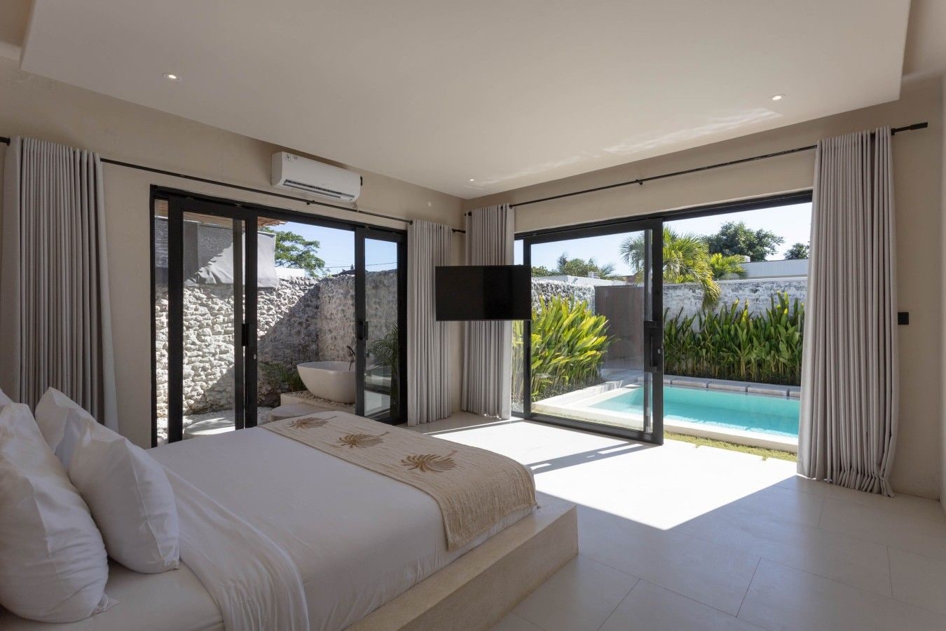 A modern bedroom with a large bed, a flat-screen TV, and a view of a swimming pool.
